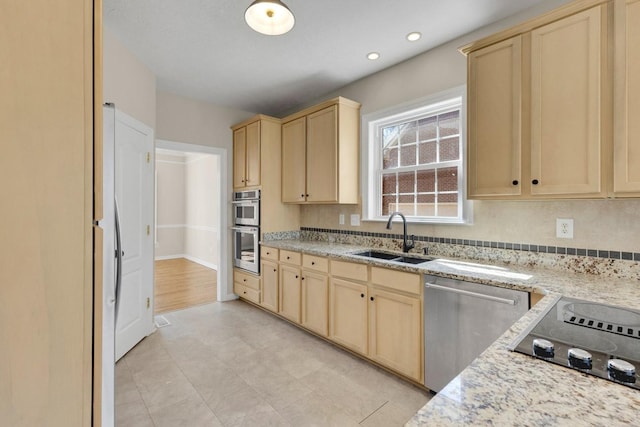 kitchen featuring light brown cabinets, appliances with stainless steel finishes, light stone counters, and a sink