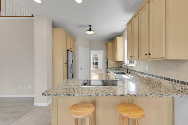 kitchen with light brown cabinetry, a sink, stainless steel fridge, a peninsula, and black electric cooktop