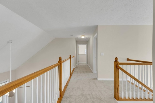 corridor featuring attic access, light carpet, a textured ceiling, an upstairs landing, and baseboards