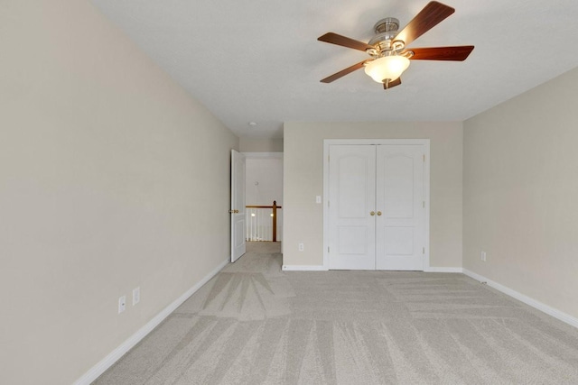 unfurnished bedroom with a closet, light colored carpet, ceiling fan, and baseboards