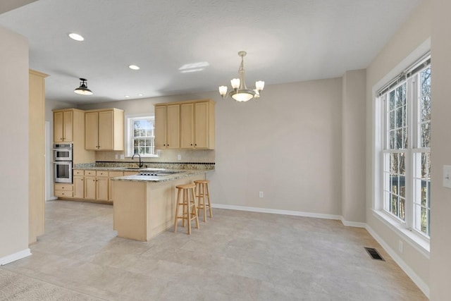 kitchen featuring visible vents, light brown cabinetry, stainless steel double oven, a sink, and a peninsula