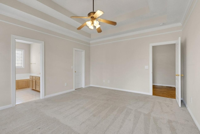 unfurnished bedroom with a raised ceiling, ensuite bathroom, ornamental molding, light carpet, and baseboards