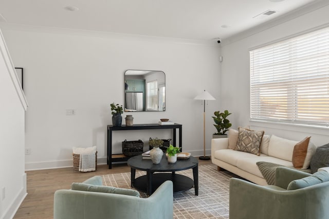 living room featuring baseboards, light wood-type flooring, visible vents, and crown molding