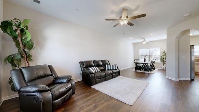 living room with baseboards, visible vents, a ceiling fan, arched walkways, and dark wood-type flooring