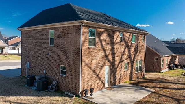 view of property exterior featuring a patio, a lawn, central AC, and brick siding