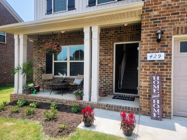 doorway to property featuring an attached garage, a porch, board and batten siding, and brick siding