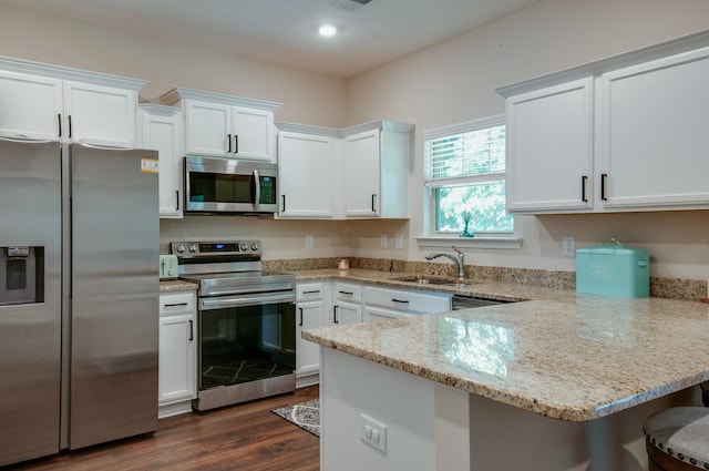 kitchen featuring appliances with stainless steel finishes, dark wood-type flooring, white cabinetry, a sink, and a peninsula