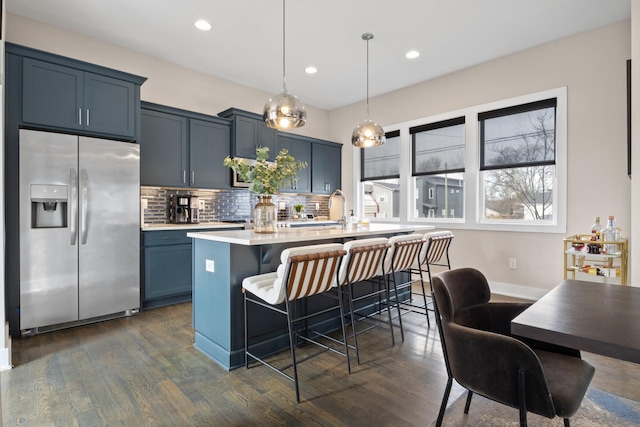 kitchen with a kitchen breakfast bar, light countertops, stainless steel refrigerator with ice dispenser, decorative backsplash, and an island with sink