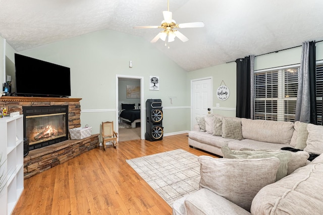 living area featuring a textured ceiling, wood finished floors, a stone fireplace, ceiling fan, and vaulted ceiling