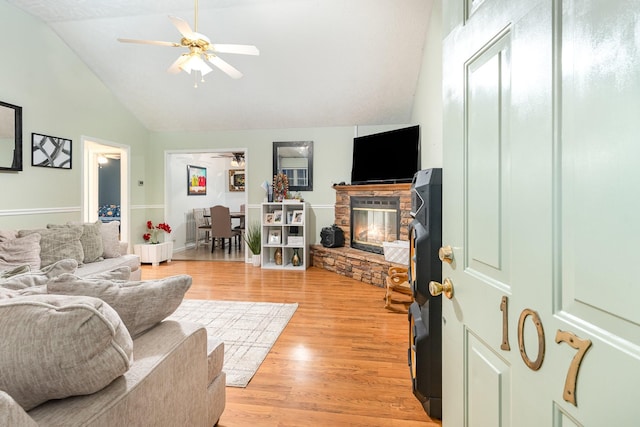 living room featuring a stone fireplace, light wood-style flooring, a ceiling fan, and high vaulted ceiling