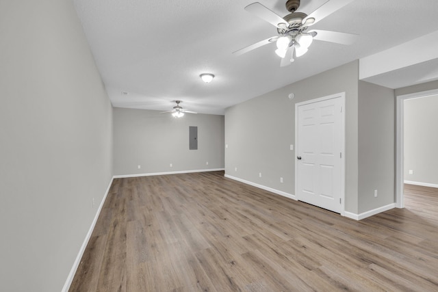 spare room with a ceiling fan, electric panel, baseboards, and wood finished floors