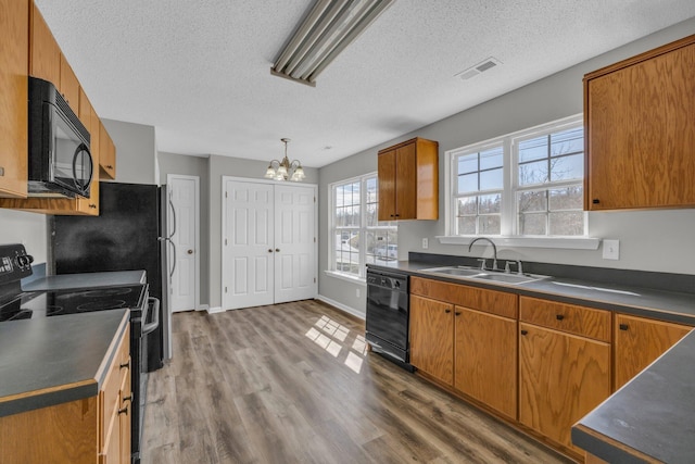 kitchen with visible vents, brown cabinetry, dark countertops, black appliances, and a sink