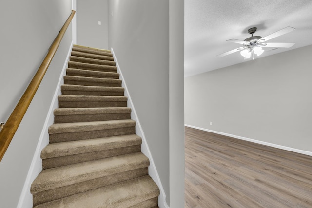 stairs featuring ceiling fan, a textured ceiling, wood finished floors, and baseboards