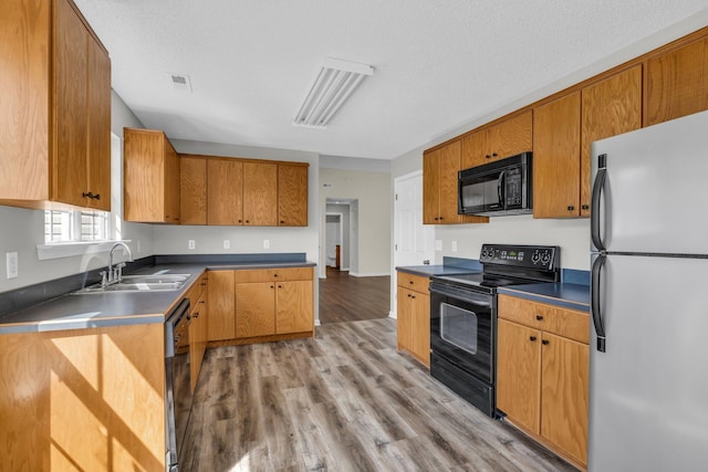 kitchen featuring visible vents, light wood-style flooring, a sink, a textured ceiling, and black appliances