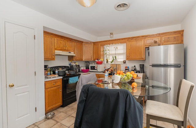 kitchen with white microwave, under cabinet range hood, black range with electric stovetop, visible vents, and freestanding refrigerator