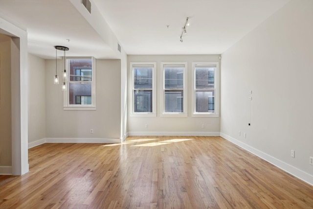 spare room with track lighting, baseboards, visible vents, and light wood finished floors