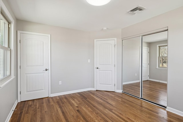 unfurnished bedroom featuring baseboards, a closet, visible vents, and wood finished floors