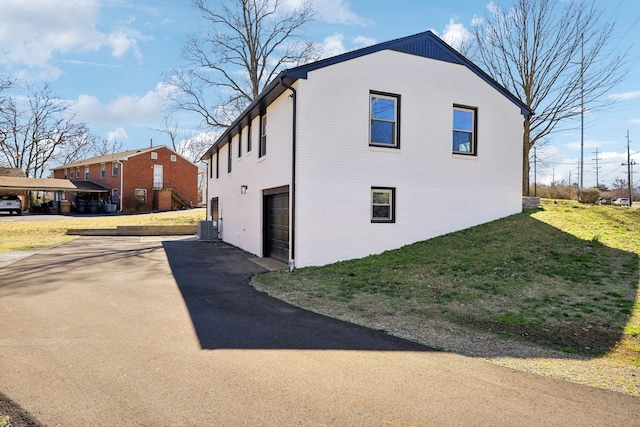 view of side of property featuring a garage, central AC, brick siding, driveway, and a yard