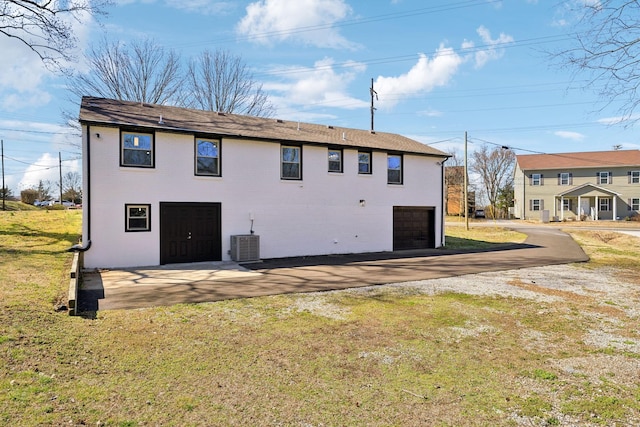 rear view of house featuring brick siding, a yard, central air condition unit, a garage, and driveway