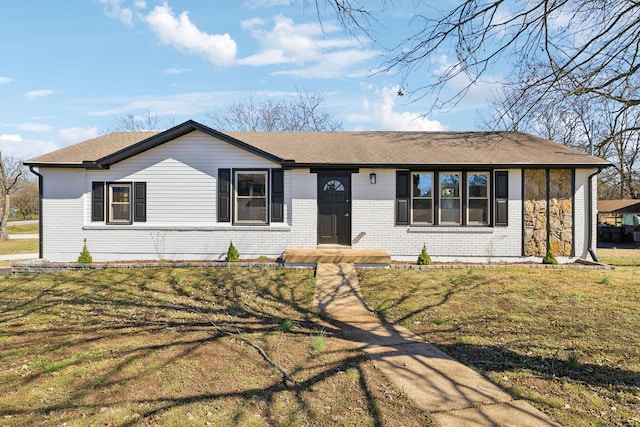 ranch-style home with a shingled roof, a front lawn, and brick siding