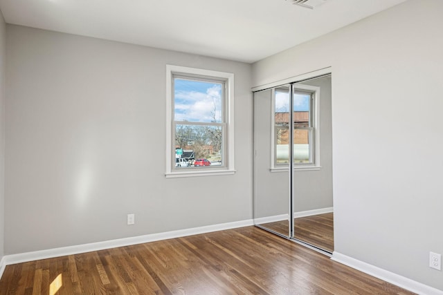 unfurnished bedroom featuring visible vents, a closet, baseboards, and wood finished floors