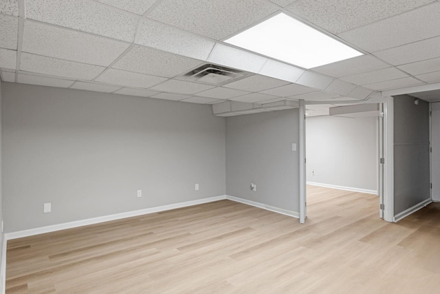 finished basement with light wood-type flooring, visible vents, a drop ceiling, and baseboards