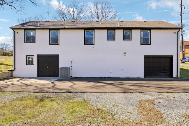 back of property with a garage, gravel driveway, central AC, and brick siding