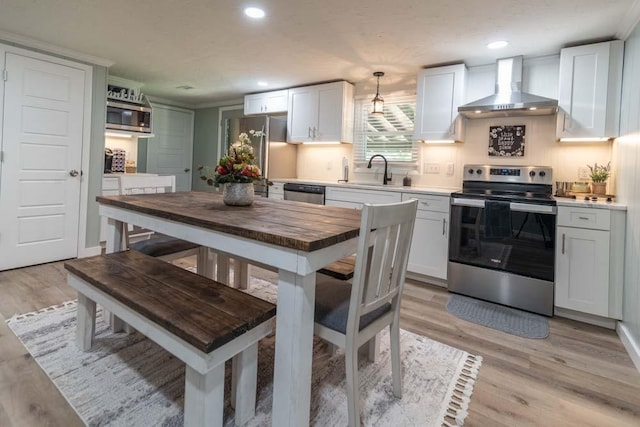 kitchen featuring appliances with stainless steel finishes, light wood-style floors, a sink, and wall chimney range hood