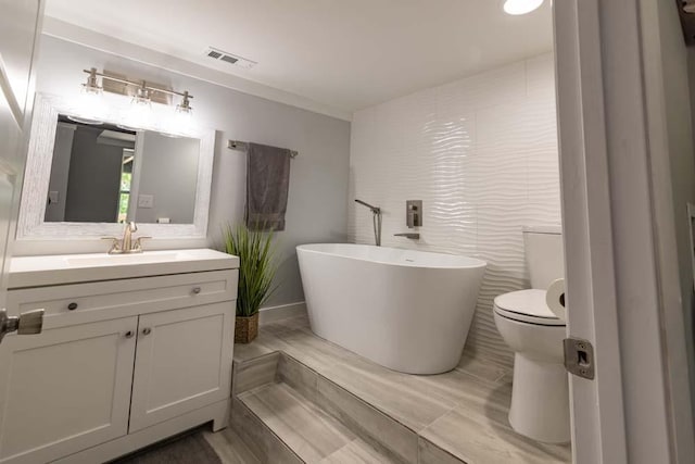 bathroom featuring visible vents, toilet, a soaking tub, vanity, and tile walls