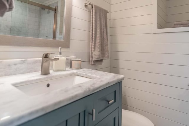 bathroom featuring a shower stall, toilet, wooden walls, and vanity