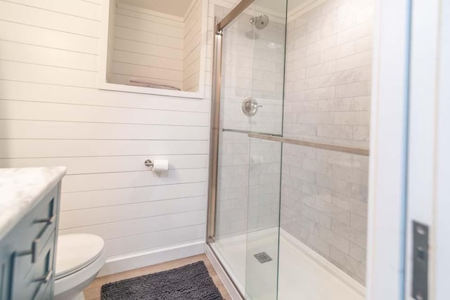 bathroom with a stall shower, vanity, toilet, and wooden walls