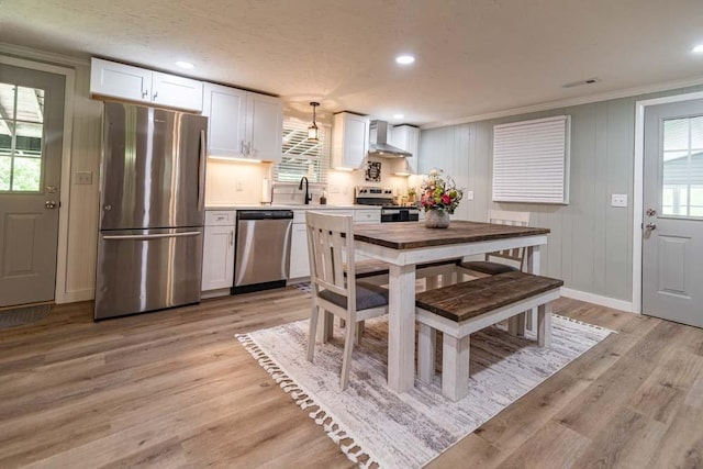 kitchen with stainless steel appliances, wall chimney range hood, light wood-type flooring, and a sink