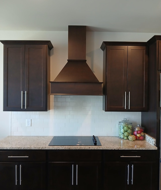 kitchen featuring light stone counters, custom range hood, and backsplash