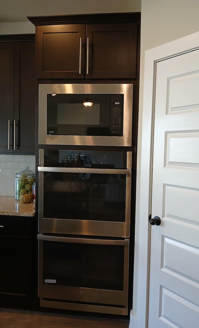 room details with stainless steel appliances, light stone counters, backsplash, and dark brown cabinetry