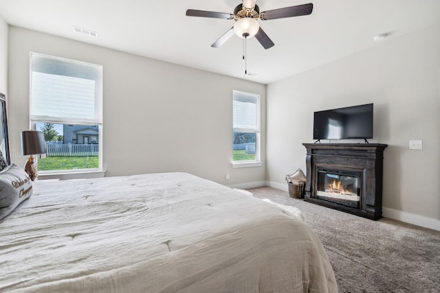 carpeted bedroom featuring ceiling fan, a glass covered fireplace, visible vents, and baseboards