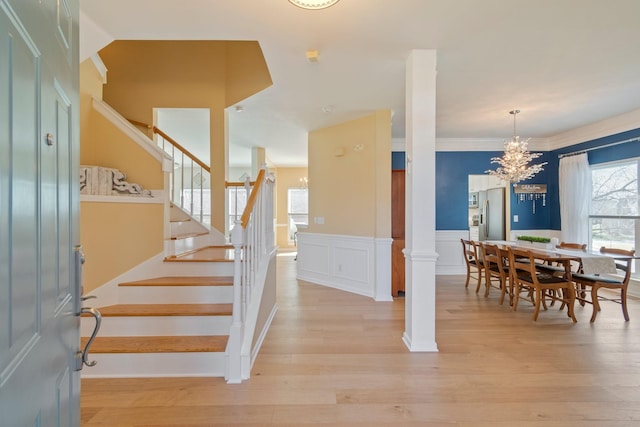 interior space featuring ornate columns, stairway, light wood finished floors, and wainscoting