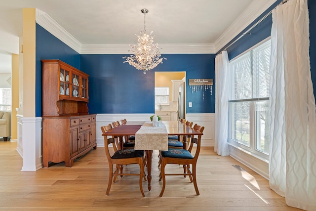 dining area with a wainscoted wall, crown molding, light wood-style flooring, and an inviting chandelier