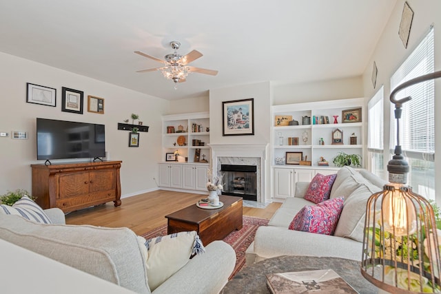 living room featuring light wood-style floors, ceiling fan, a fireplace, and baseboards