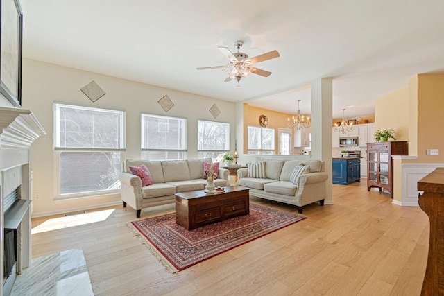 living area with a fireplace, light wood finished floors, and ceiling fan with notable chandelier