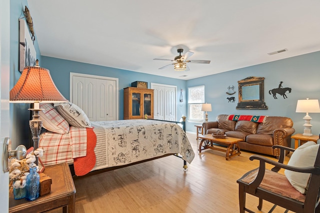 bedroom featuring ceiling fan, visible vents, multiple closets, and wood finished floors