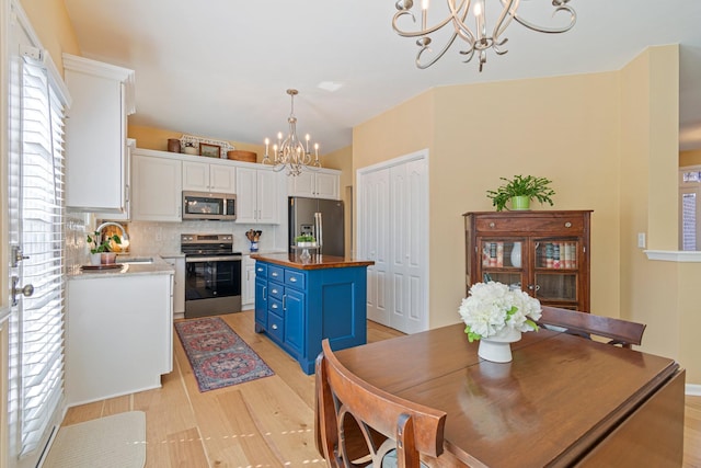 kitchen featuring a notable chandelier, butcher block counters, white cabinets, blue cabinetry, and appliances with stainless steel finishes