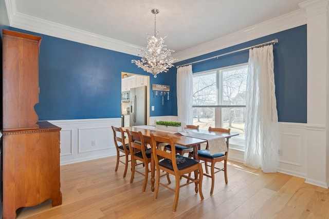 dining area with a chandelier, light wood-type flooring, a wainscoted wall, and crown molding