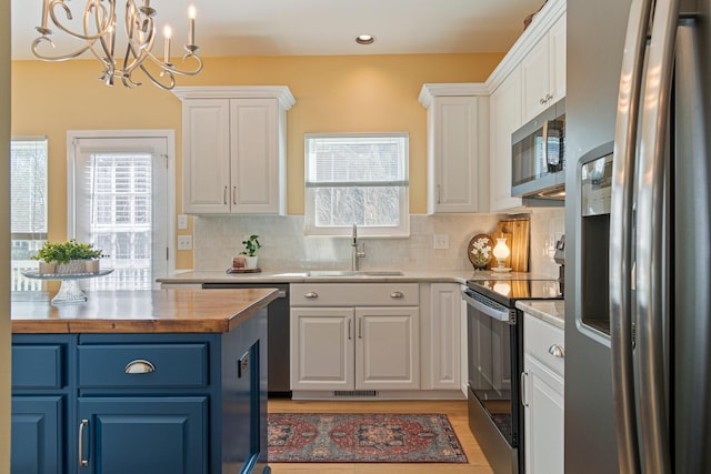 kitchen with a sink, wood counters, white cabinetry, blue cabinetry, and appliances with stainless steel finishes