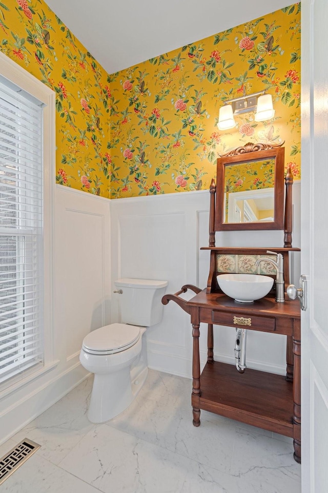 half bath featuring wallpapered walls, visible vents, marble finish floor, and wainscoting