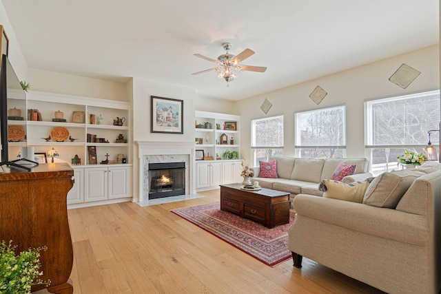 living room with light wood-style floors, ceiling fan, a fireplace, and built in features