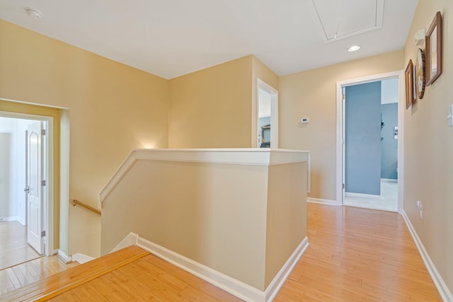 hall with light wood finished floors, attic access, baseboards, and an upstairs landing