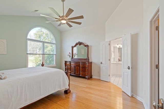 bedroom featuring light wood finished floors, visible vents, connected bathroom, vaulted ceiling, and baseboards