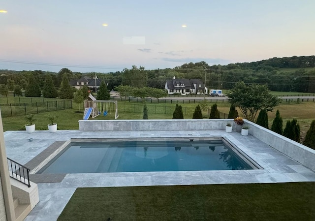 view of swimming pool featuring a fenced backyard, a fenced in pool, a lawn, and a playground