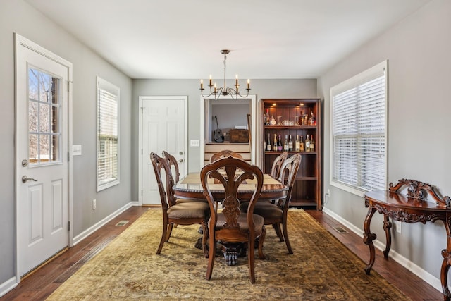 dining space featuring an inviting chandelier, visible vents, baseboards, and dark wood-style flooring