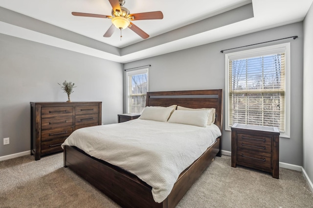 carpeted bedroom featuring a tray ceiling, a ceiling fan, and baseboards